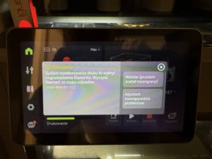 Ostrzeżenie AI na ekranie drukarki Bambu Lab P2S informujące o nagromadzeniu filamentu i konieczności oczyszczenia zsypu odpadów